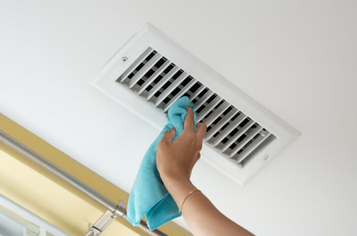 Person cleaning ceiling vent with blue cloth