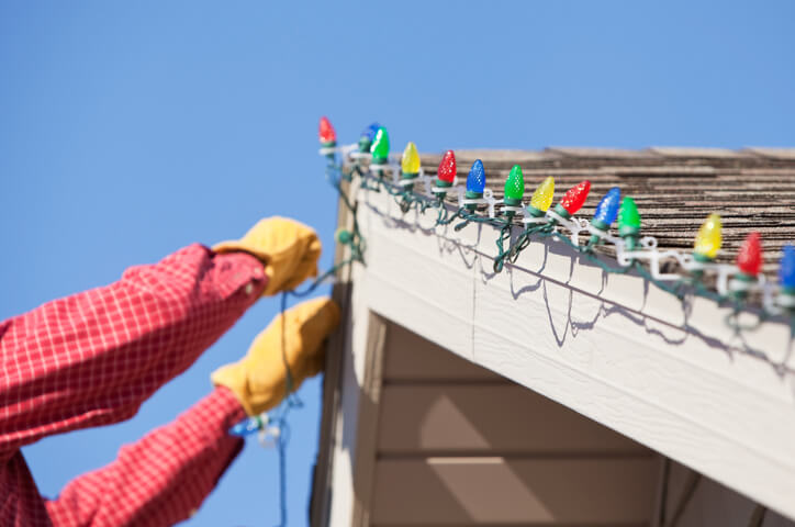 Person adding Christmas lights to roof